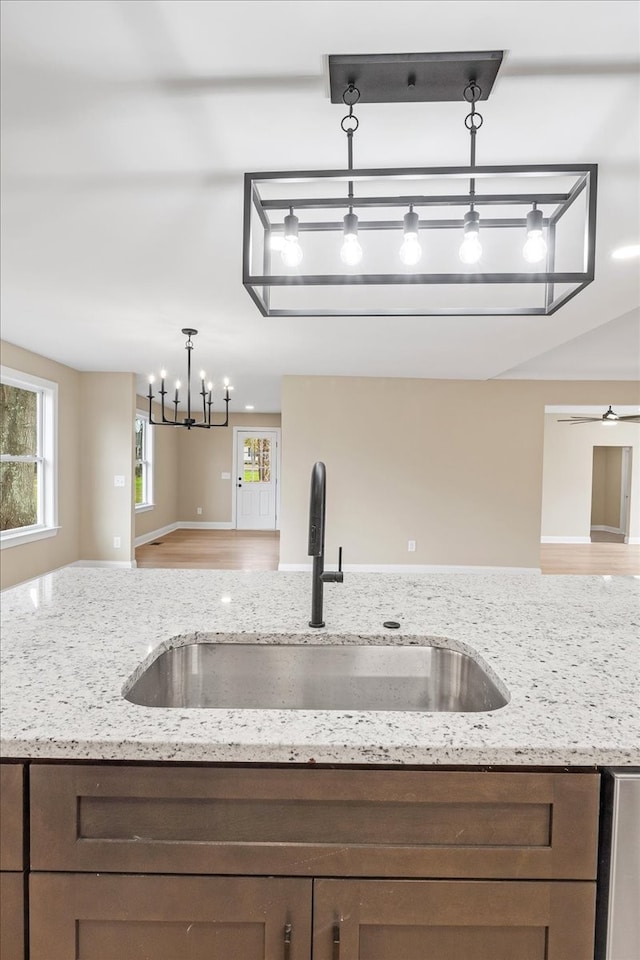 kitchen featuring ceiling fan with notable chandelier, sink, hanging light fixtures, light hardwood / wood-style flooring, and light stone counters