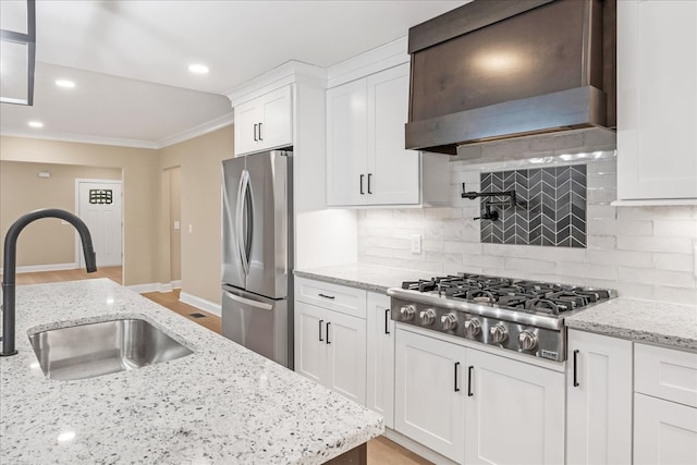 kitchen with light stone countertops, premium range hood, stainless steel appliances, sink, and white cabinets