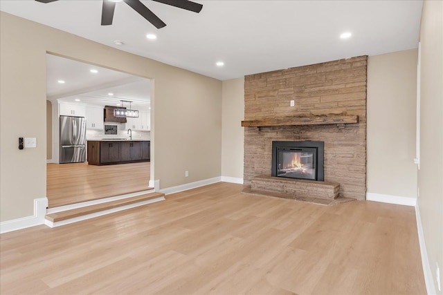 unfurnished living room featuring ceiling fan, light hardwood / wood-style floors, sink, and a fireplace