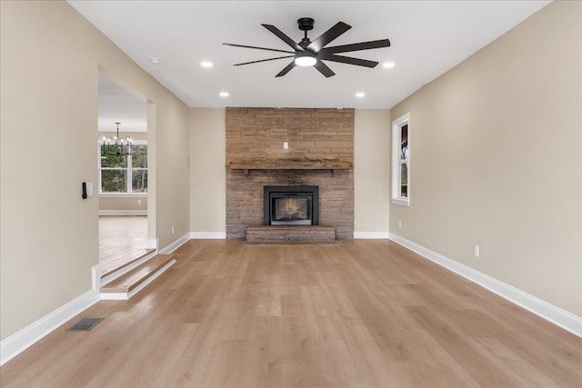 unfurnished living room with a fireplace, light wood-type flooring, and ceiling fan with notable chandelier