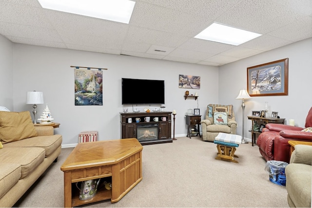 living room featuring a drop ceiling, light colored carpet, visible vents, baseboards, and a glass covered fireplace