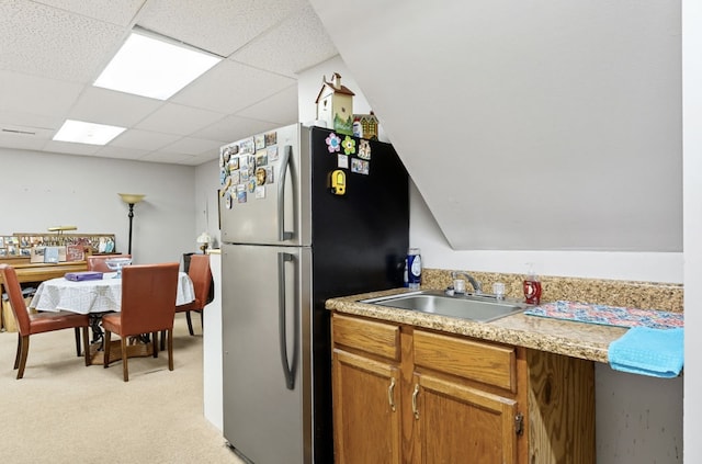 kitchen featuring light carpet, a drop ceiling, freestanding refrigerator, light countertops, and a sink