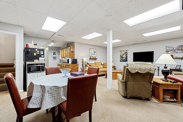 dining area with light carpet, stairway, and a paneled ceiling