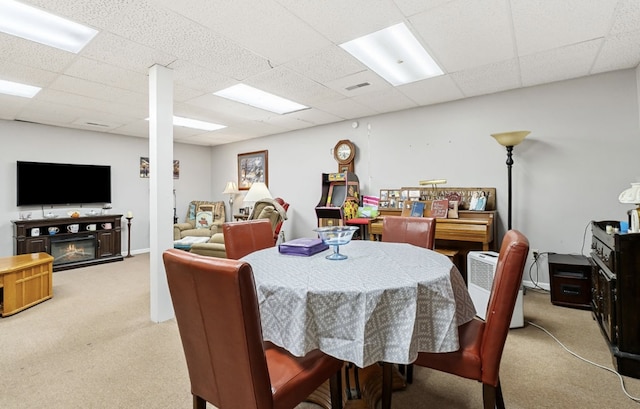 dining space with a drop ceiling, a glass covered fireplace, visible vents, and light colored carpet