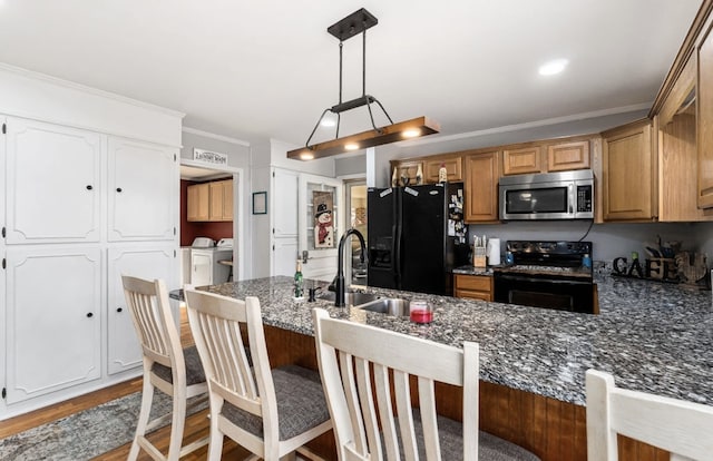 kitchen featuring light wood finished floors, washing machine and clothes dryer, a peninsula, crown molding, and black appliances