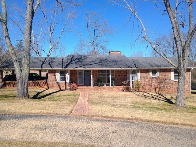 ranch-style house with a front yard, a chimney, a porch, and brick siding