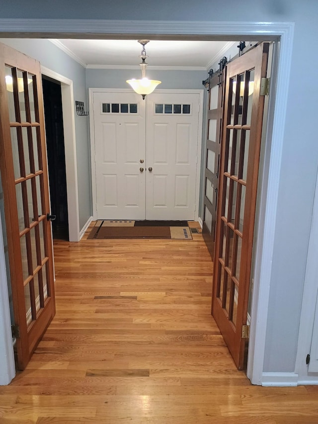 foyer featuring light wood-type flooring, a barn door, baseboards, and crown molding