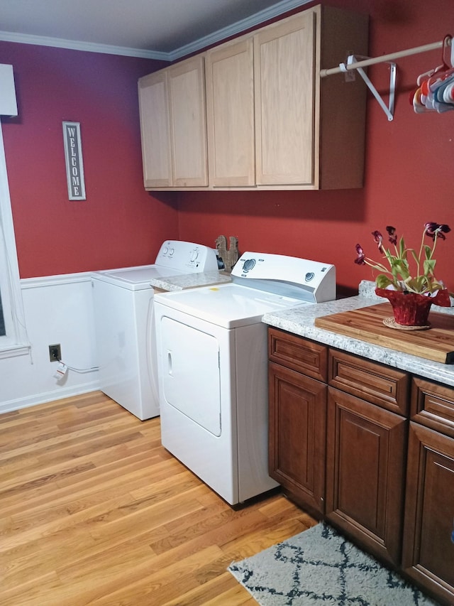 laundry area featuring light wood-style flooring, a wainscoted wall, cabinet space, washer and clothes dryer, and crown molding