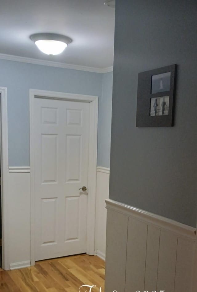 corridor with wainscoting, crown molding, and light wood finished floors