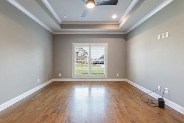 empty room featuring ceiling fan, a raised ceiling, wood-type flooring, and crown molding