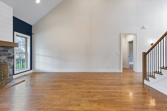 unfurnished living room with a stone fireplace, wood-type flooring, and high vaulted ceiling