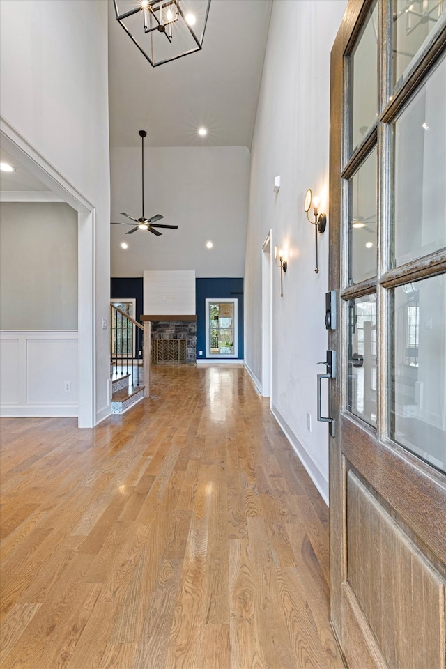 foyer featuring radiator heating unit, a stone fireplace, high vaulted ceiling, ceiling fan with notable chandelier, and light wood-type flooring