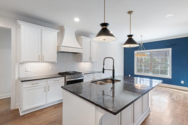 kitchen with sink, an island with sink, decorative light fixtures, custom range hood, and stainless steel range with gas stovetop