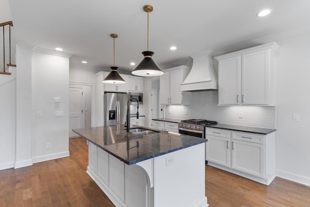 kitchen with sink, an island with sink, light hardwood / wood-style floors, custom range hood, and stainless steel appliances