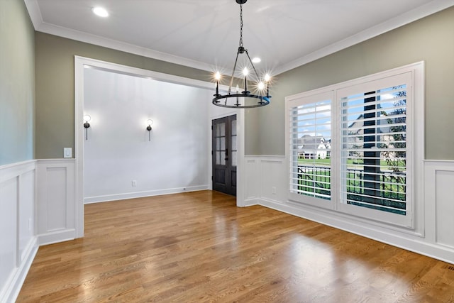 unfurnished dining area featuring ornamental molding, light wood-type flooring, and a notable chandelier