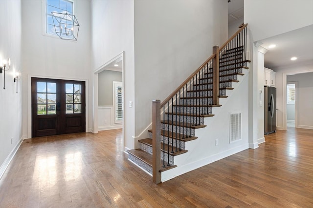 foyer with wood-type flooring, a towering ceiling, and french doors