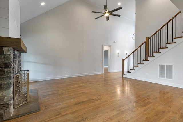 unfurnished living room with a stone fireplace, ceiling fan, high vaulted ceiling, and wood-type flooring