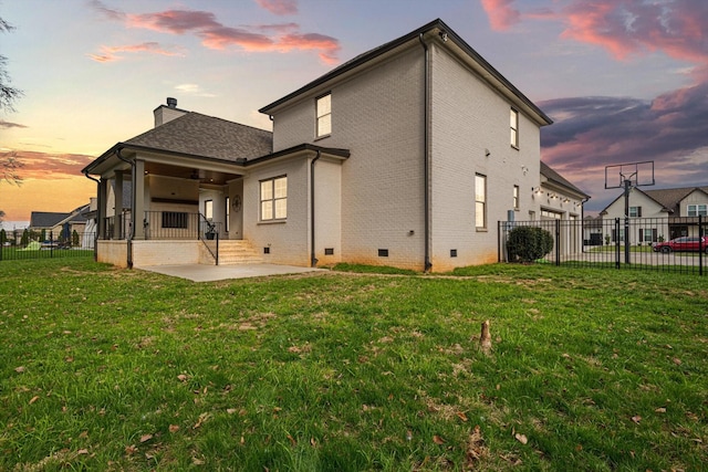 back house at dusk featuring a lawn and a patio