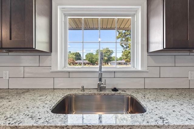 room details with dark brown cabinets, backsplash, light stone counters, and sink