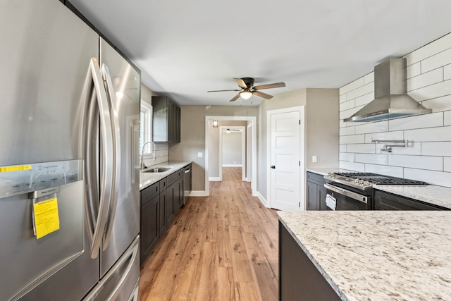 kitchen featuring wall chimney range hood, sink, light hardwood / wood-style flooring, decorative backsplash, and stainless steel appliances