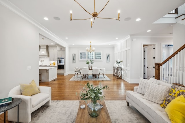 living room with ceiling fan with notable chandelier, light wood-type flooring, and crown molding