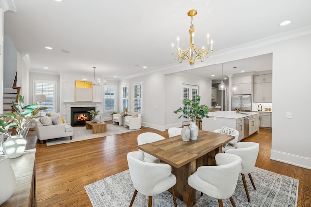 dining space featuring an inviting chandelier, sink, crown molding, light hardwood / wood-style flooring, and a large fireplace