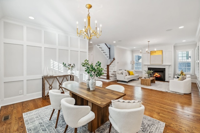 dining space featuring wood-type flooring, ornamental molding, and an inviting chandelier