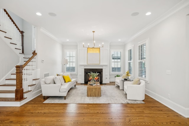 living room featuring a chandelier, crown molding, a fireplace, and light hardwood / wood-style floors