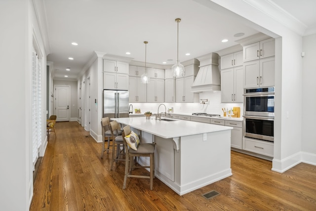 kitchen with premium range hood, hardwood / wood-style flooring, an island with sink, and appliances with stainless steel finishes