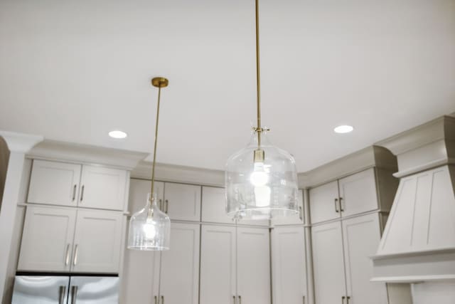 interior details with decorative light fixtures, stainless steel fridge, and white cabinetry