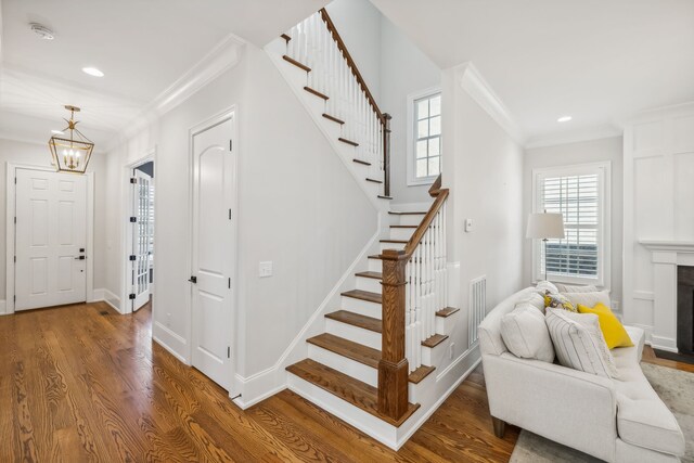 stairs featuring wood-type flooring, an inviting chandelier, and ornamental molding