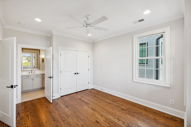 unfurnished bedroom featuring ceiling fan, crown molding, sink, hardwood / wood-style floors, and a closet