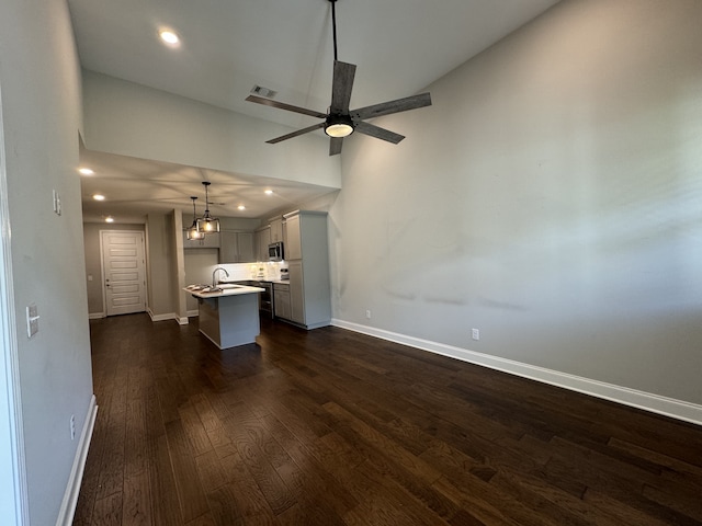 unfurnished living room with dark hardwood / wood-style flooring, a high ceiling, and ceiling fan with notable chandelier