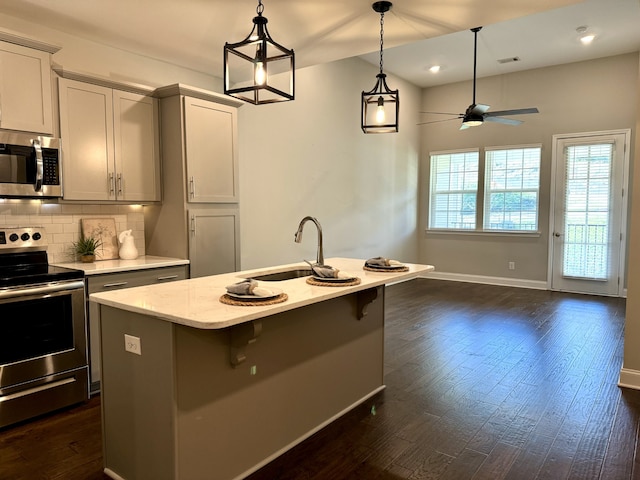 kitchen featuring a kitchen island with sink, sink, ceiling fan, appliances with stainless steel finishes, and dark hardwood / wood-style flooring