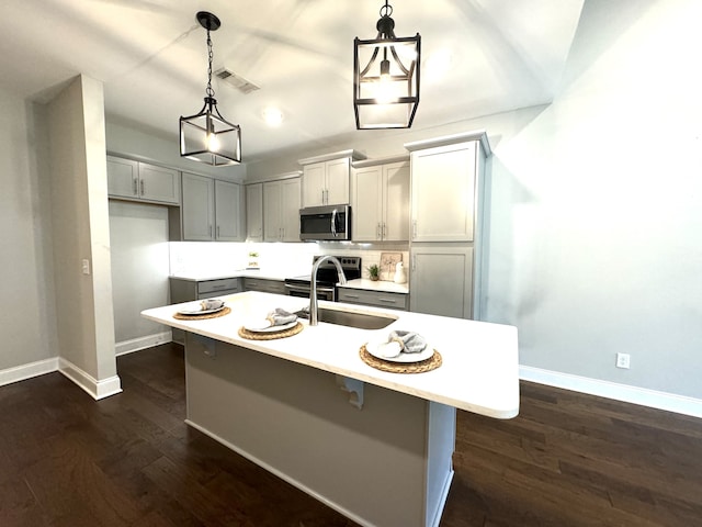 kitchen with gray cabinetry, stainless steel appliances, a center island with sink, dark hardwood / wood-style flooring, and decorative light fixtures