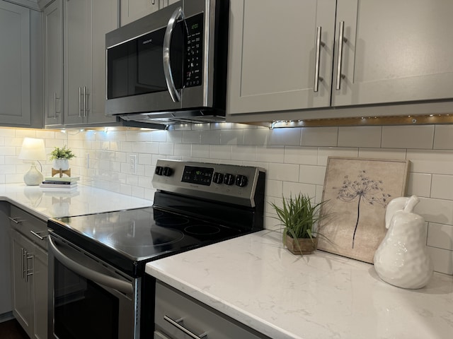 kitchen with light stone countertops, gray cabinetry, decorative backsplash, and stainless steel appliances