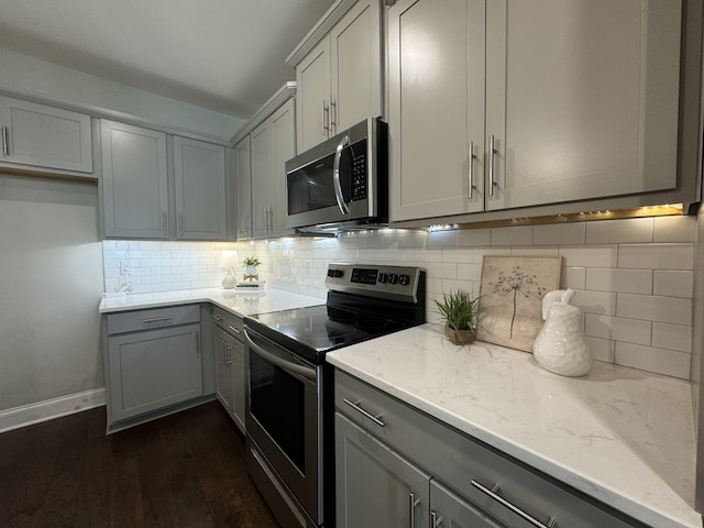 kitchen with dark wood-type flooring, appliances with stainless steel finishes, gray cabinets, and tasteful backsplash