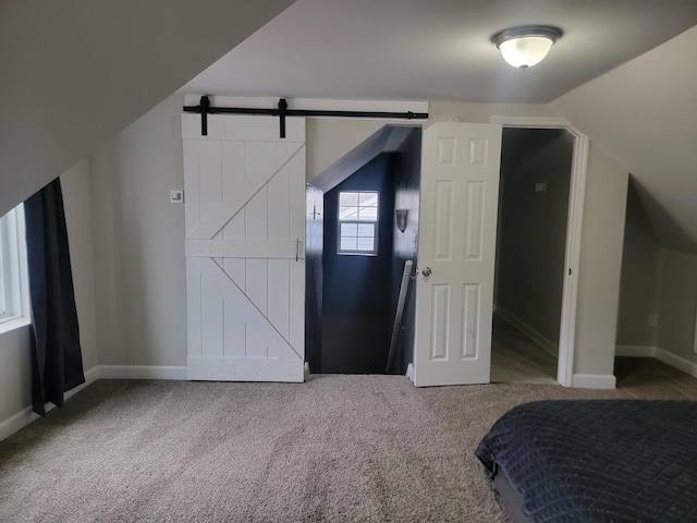 bedroom featuring a barn door, lofted ceiling, and carpet flooring