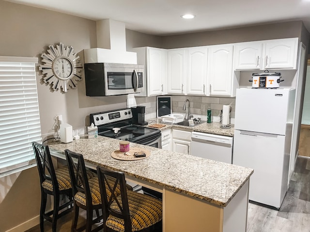 kitchen featuring appliances with stainless steel finishes, light stone counters, light hardwood / wood-style flooring, white cabinets, and a breakfast bar area