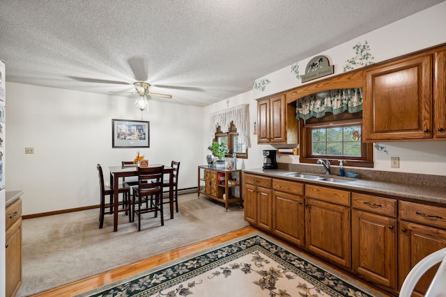 kitchen with a textured ceiling, ceiling fan, sink, and light hardwood / wood-style flooring