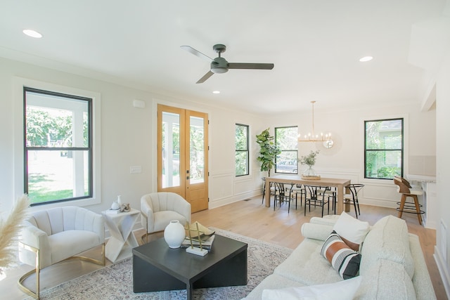 living room with french doors, ceiling fan with notable chandelier, light hardwood / wood-style flooring, and crown molding