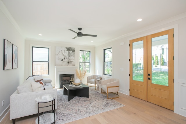 living room with french doors, ornamental molding, ceiling fan, a tile fireplace, and light hardwood / wood-style floors