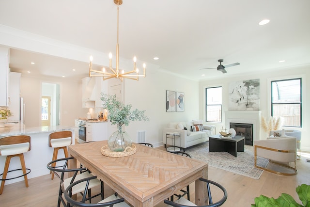 dining room with ceiling fan with notable chandelier, crown molding, sink, a fireplace, and light hardwood / wood-style floors