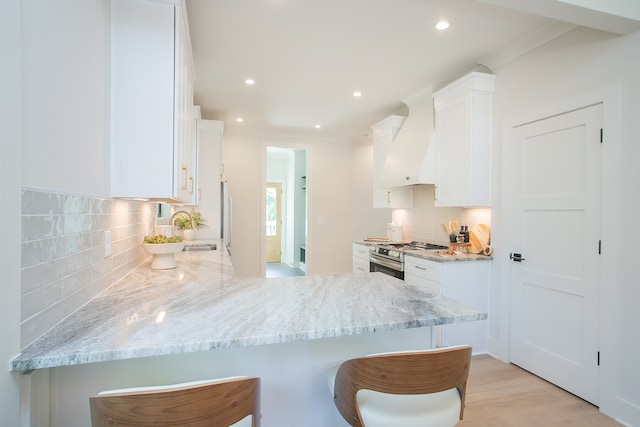 kitchen featuring kitchen peninsula, a kitchen breakfast bar, premium range hood, stainless steel range, and white cabinetry