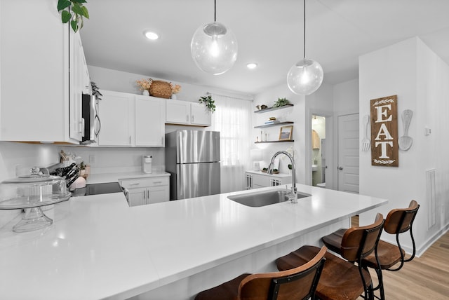 kitchen featuring kitchen peninsula, stainless steel appliances, sink, decorative light fixtures, and light hardwood / wood-style floors