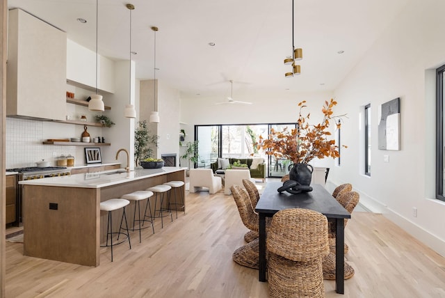 dining room with sink, high vaulted ceiling, ceiling fan, and light hardwood / wood-style flooring