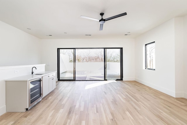 interior space with light hardwood / wood-style floors, ceiling fan, indoor wet bar, and wine cooler