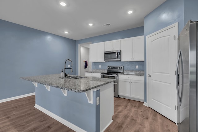 kitchen featuring stainless steel appliances, a kitchen breakfast bar, light stone counters, a kitchen island with sink, and white cabinets