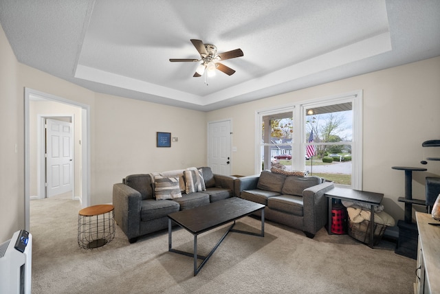 living room with ceiling fan, light carpet, and a tray ceiling