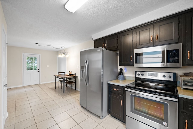 kitchen with light tile patterned floors, a textured ceiling, stainless steel appliances, and a notable chandelier